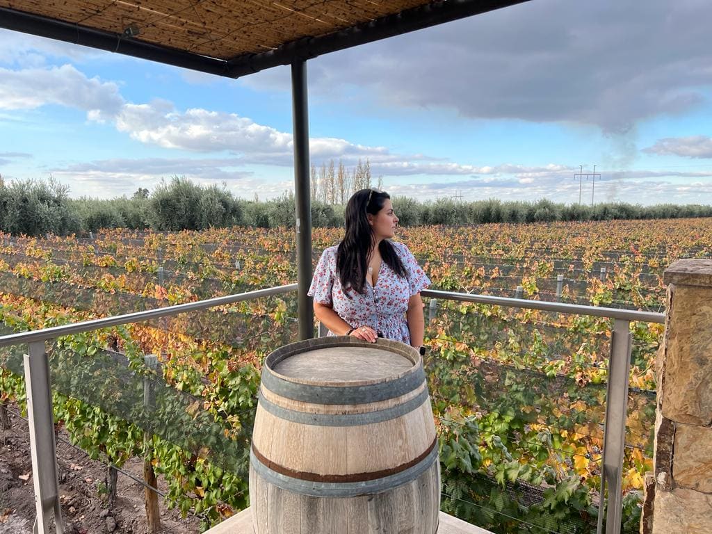 Woman stood behind a wine barrel, with a vineyard in the background in Mendoza, Argentina