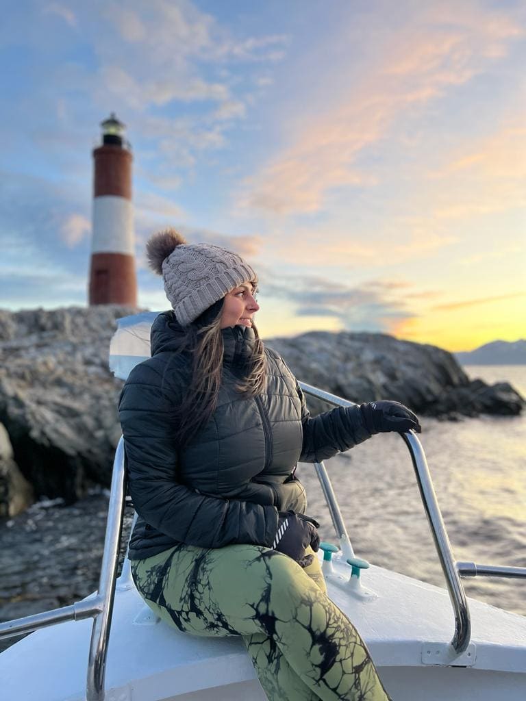 Woman on boat in front of a lighthouse at sunset