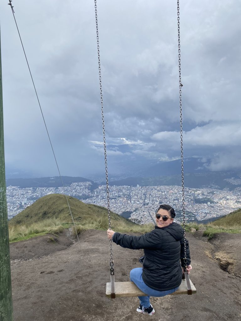 A woman sitting on a swing looking back over shoulder in front of a view overlooking Quito, Ecuador