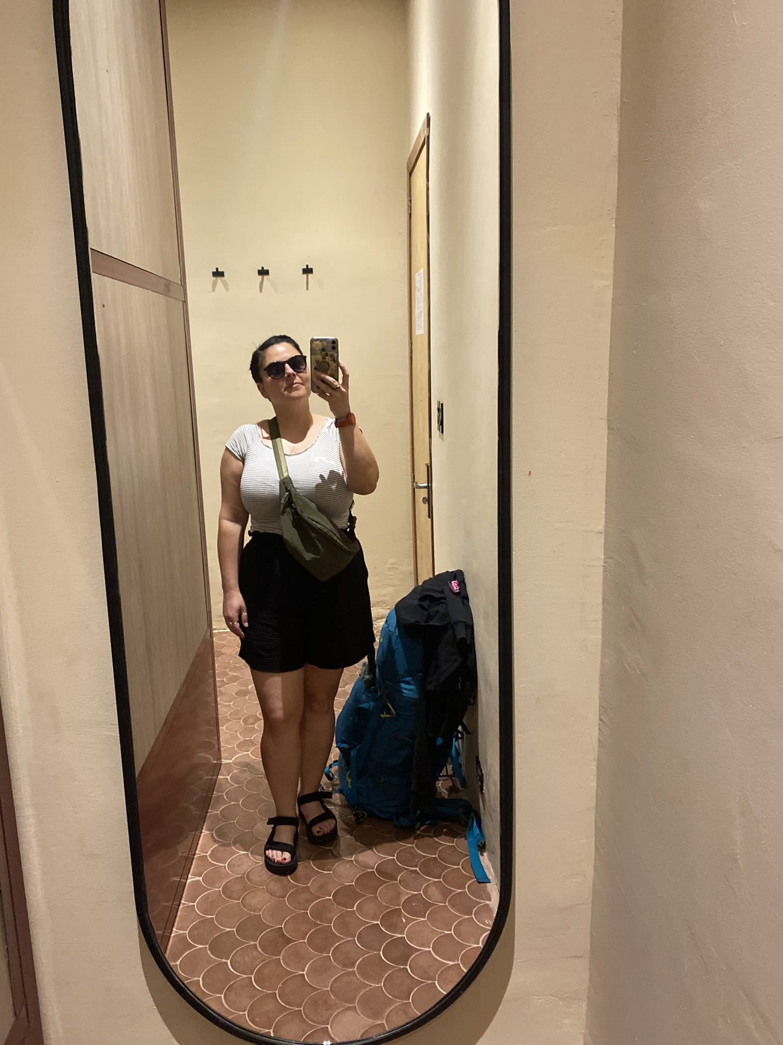 Woman taking a photograph in the mirror of her reflection with her backpack beside her.
