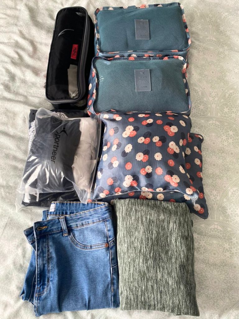 Packing cubes and clothes laid out on a bed.