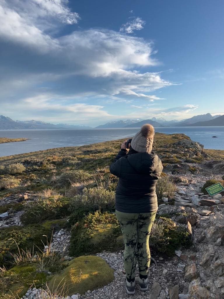 Woman with her back to the camera taking a photograph of the Beagle Channel and mountains in Ushuaia, Argentina.